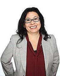 Claudia Santellano stands in front of a white background and smiles at the camera.
